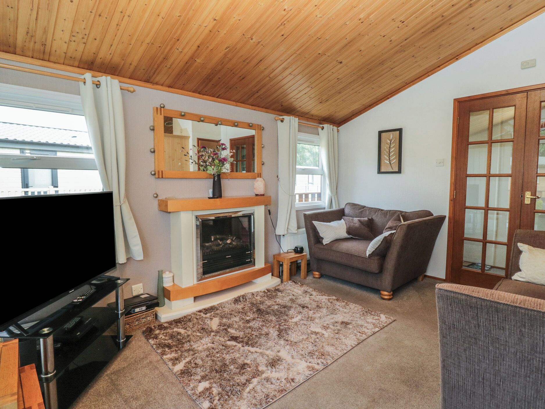 Una sala de estar acogedora con chimenea, un sofá, un televisor y techo de madera.