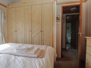 A bedroom with a bed, a wooden wardrobe, and a door leading to a bathroom. - The Cedars (Carnforth)