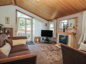 A furnished living room with a sofa, television, fireplace, and a view of the outdoors. - The Cedars (Carnforth)