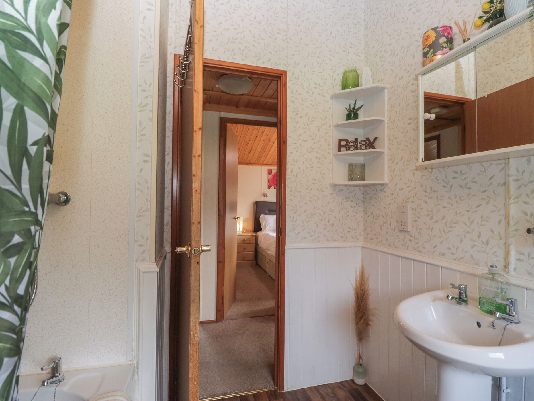Un baño con lavamanos blanco, un espejo y una repisa con un adorno.