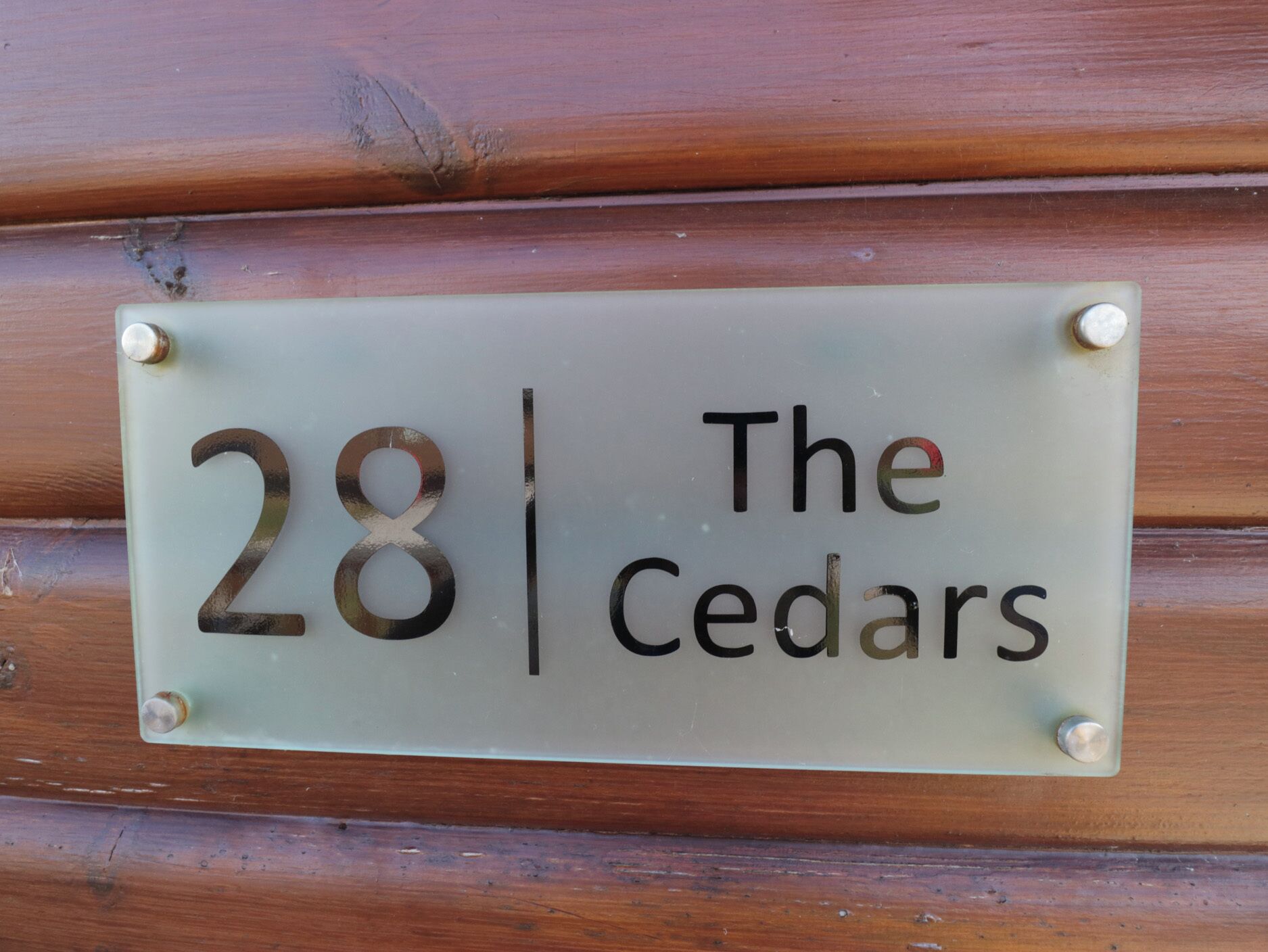 Une plaque de numéro de maison portant le numéro 28 et le nom « The Cedars », fixée à un mur en bois.