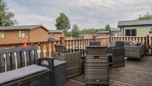 A deck with wicker furniture and a bench, surrounded by a wooden fence. - The Cedars (Carnforth)