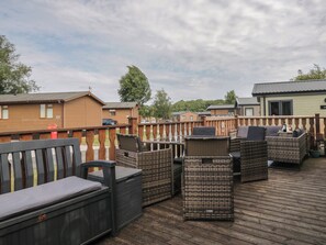 A deck with wicker furniture and a bench, surrounded by a wooden fence. - The Cedars (Carnforth)
