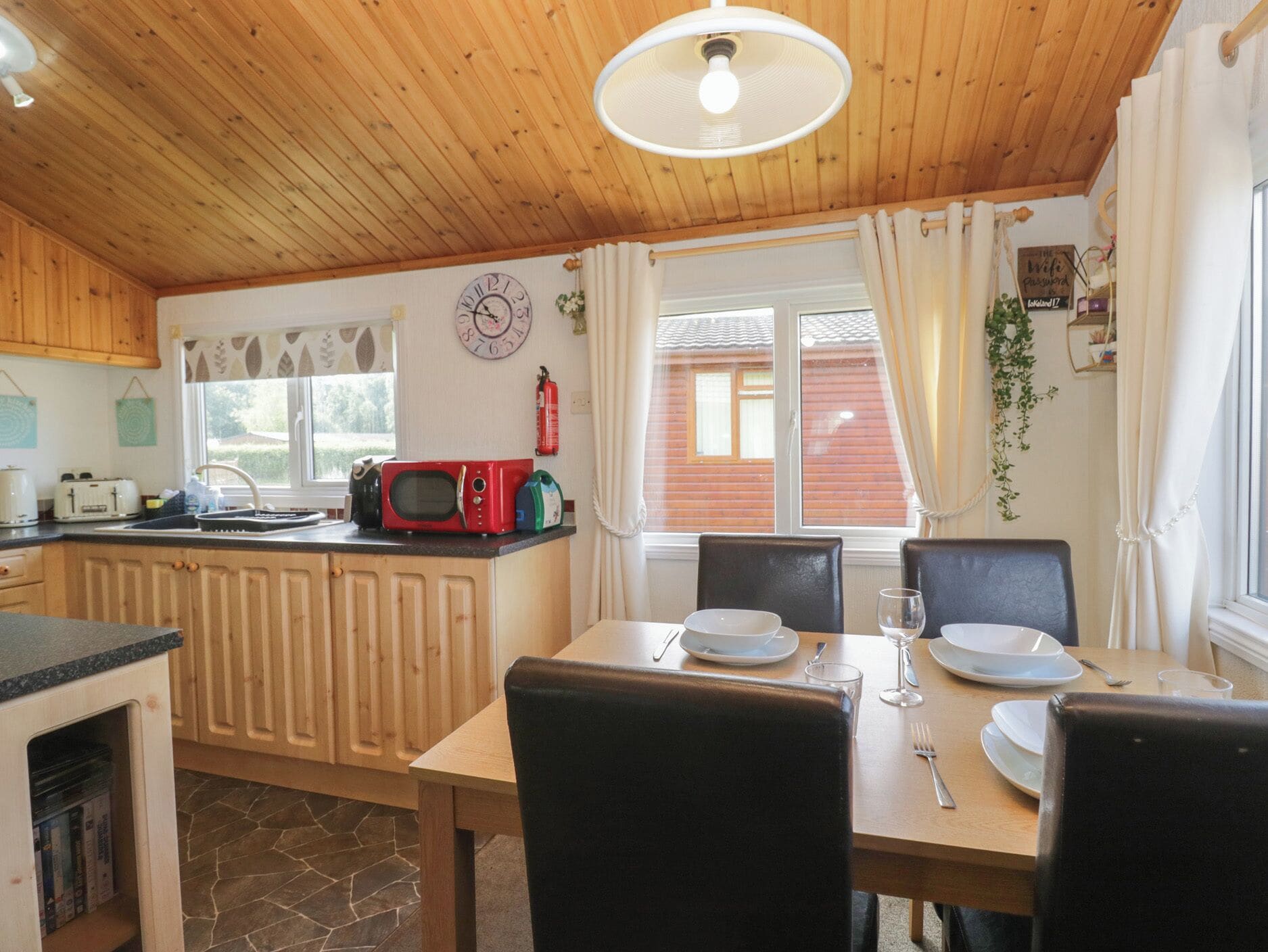 A wooden interior with a kitchen, dining area, and a window with curtains.