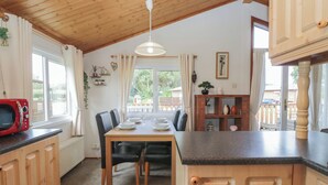 A kitchen with wooden cabinets, a dining table with chairs, a microwave, and a hanging light fixture. - The Cedars (Carnforth)