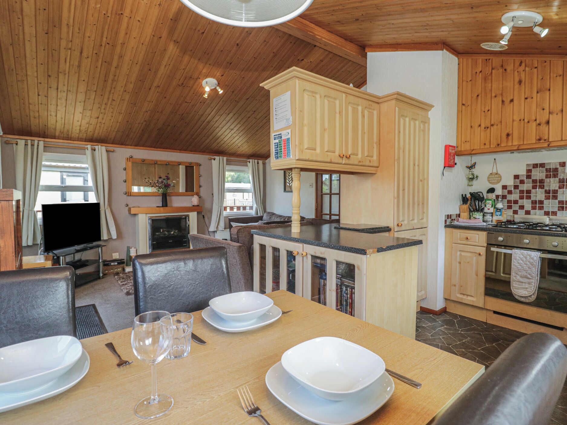 A cozy kitchen with wooden cabinets, a dining table set for two, and a television in the background.
