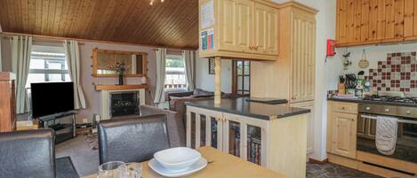 A cozy kitchen with wooden cabinets, a dining table set for two, and a television in the background.