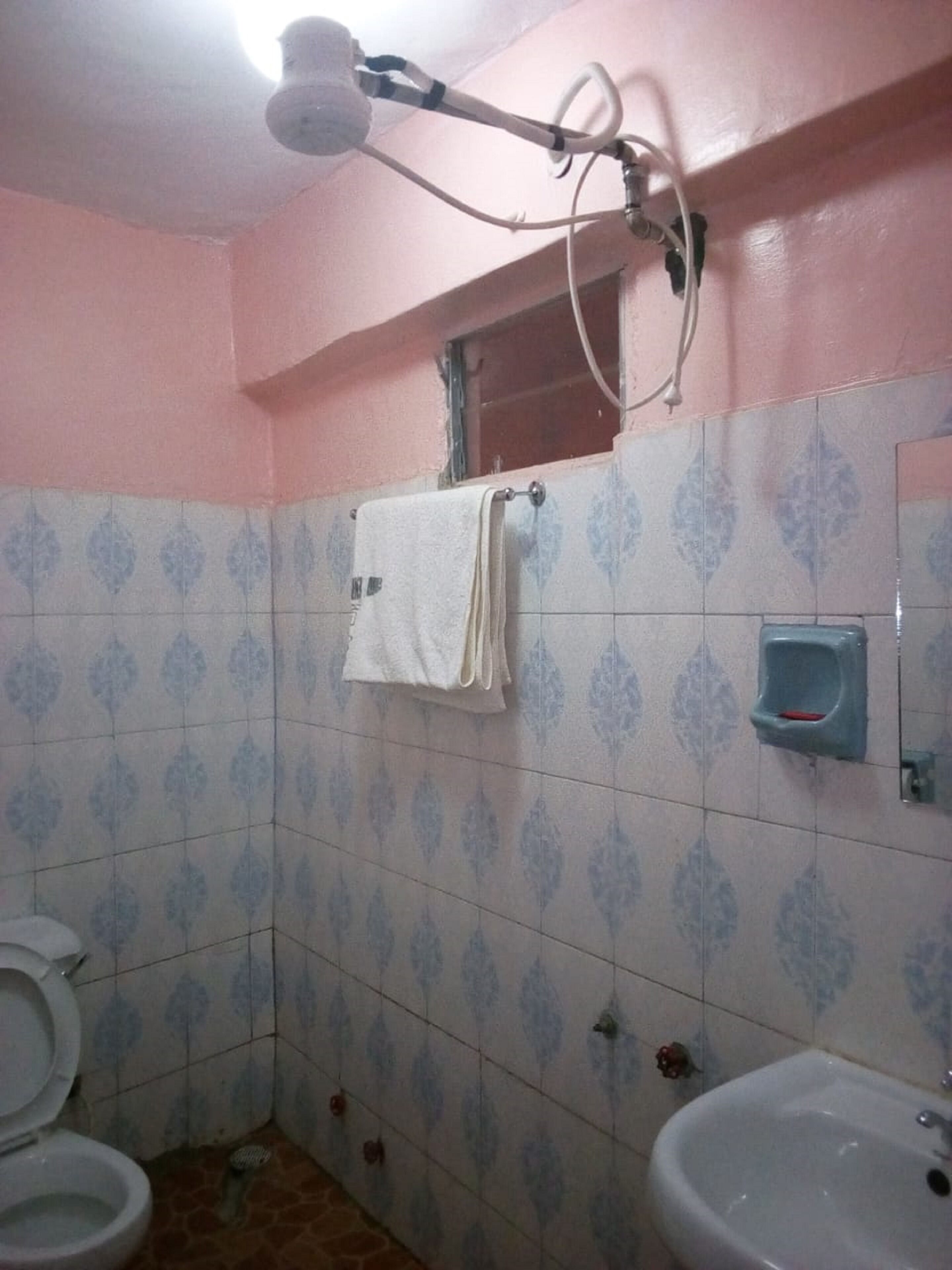A bathroom with a toilet, bidet, and sink. There is a towel hanging on the wall and a showerhead above the sink.