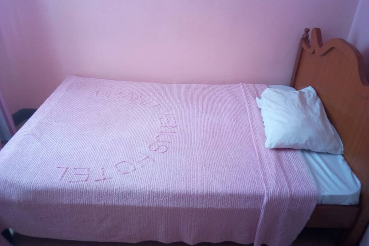 Ein Einzelbett mit pinker Bettdecke und einem weißen Kopfkissen in einem Zimmer mit rosafarbenen Wänden.
