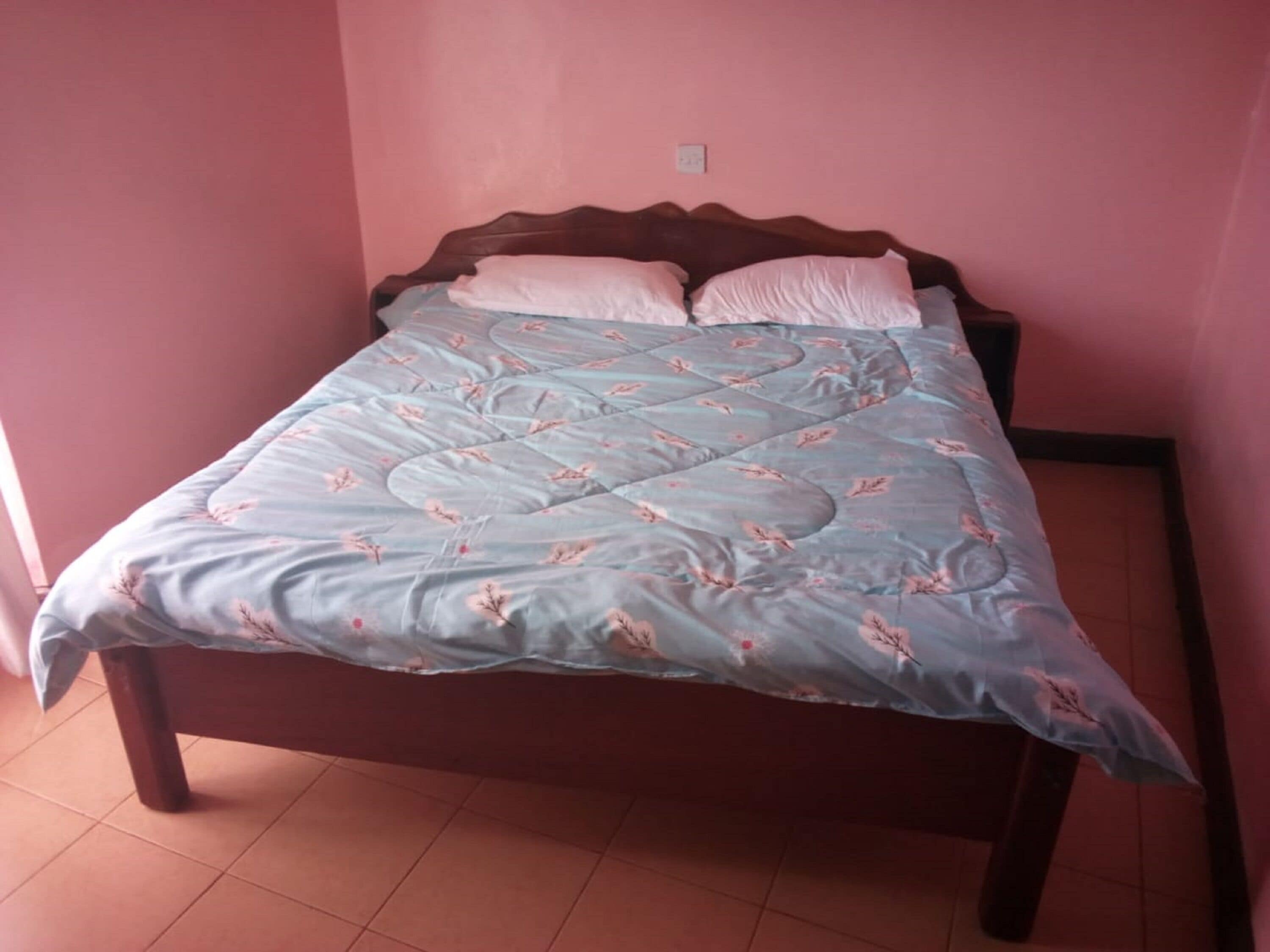 A bed with a floral-patterned bedspread and pillows, a wooden headboard, and a tiled floor.