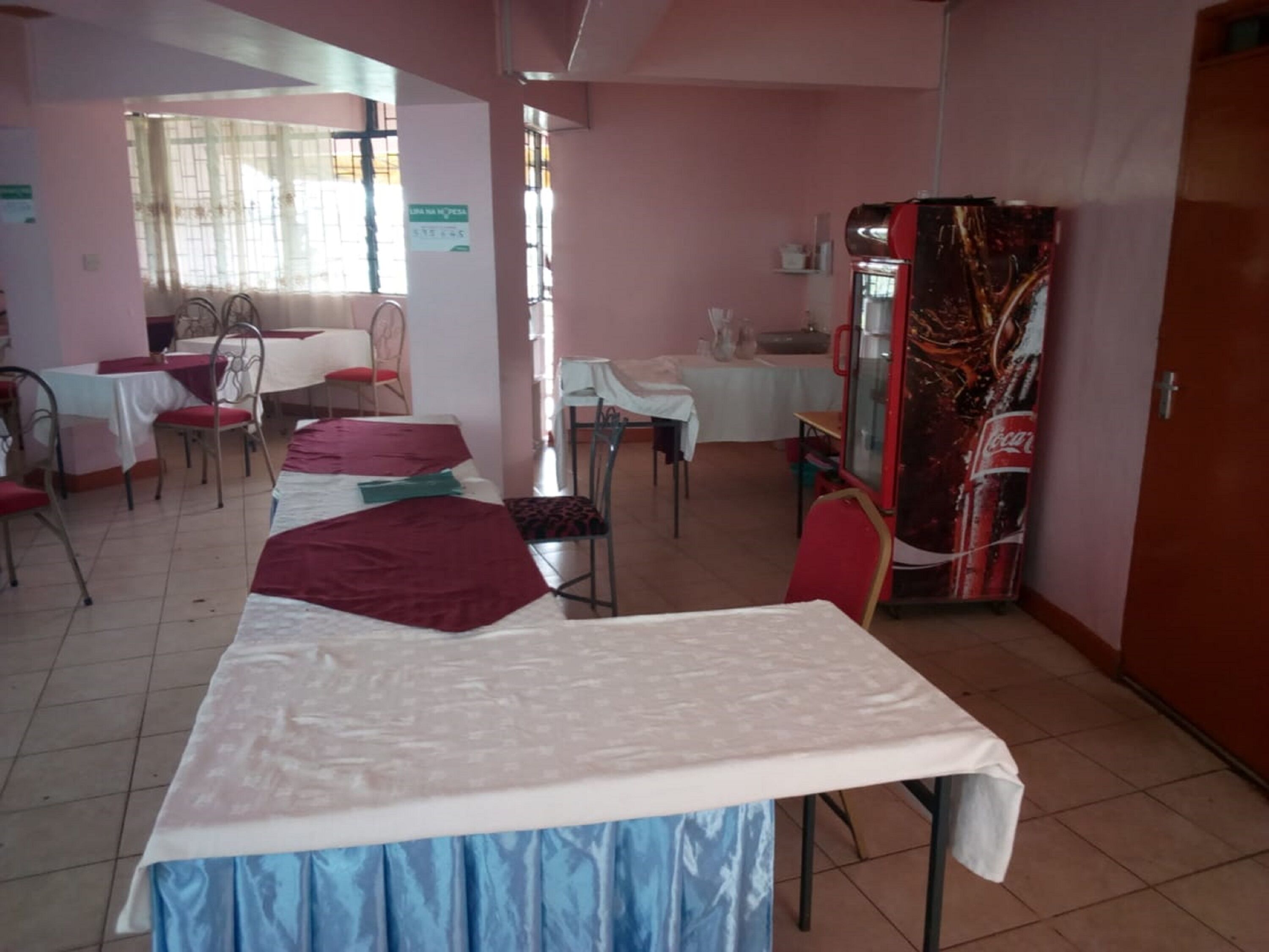 Habitación de hotel con cama, mesa de comedor, sillas, refrigerador y ventana con cortinas.
