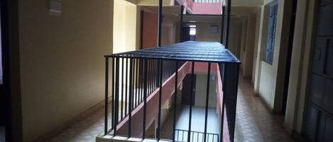 Un pasillo con una escalera que lleva a una plataforma, suelo de baldosas y una puerta al final.