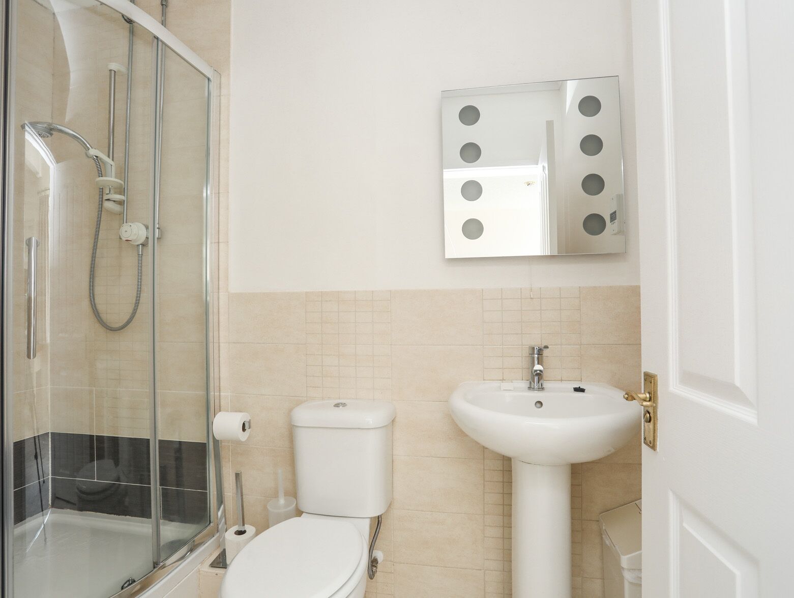 A bathroom with a glass-enclosed shower, a toilet, a sink, and a mirror with circular cutouts.