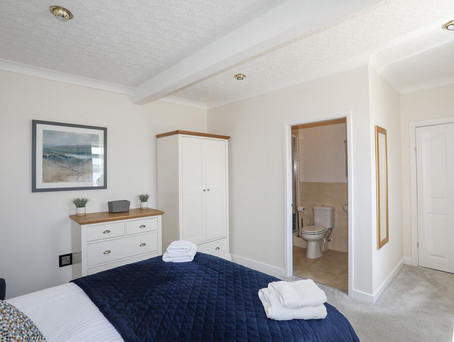 Een slaapkamer met een bed, een kledingkast, een badkamer die door een geopende deur zichtbaar is en een lijst met een afbeelding aan de muur.