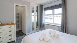 A hotel room with a bed, a dresser, a mirror, and a window with curtains. - Sea Pebbles (Weymouth)
