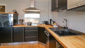 A modern kitchen with a wooden countertop, black cabinets, a stainless steel range hood, and a built-in oven. - Sea Pebbles (Weymouth)