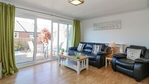 A living room with a black leather sofa, a white coffee table, and a glass door leading to a patio. - Sea Pebbles (Weymouth)