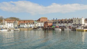 A harbor with boats docked, buildings along the waterfront, and a clear sky. - Sea Pebbles (Weymouth)