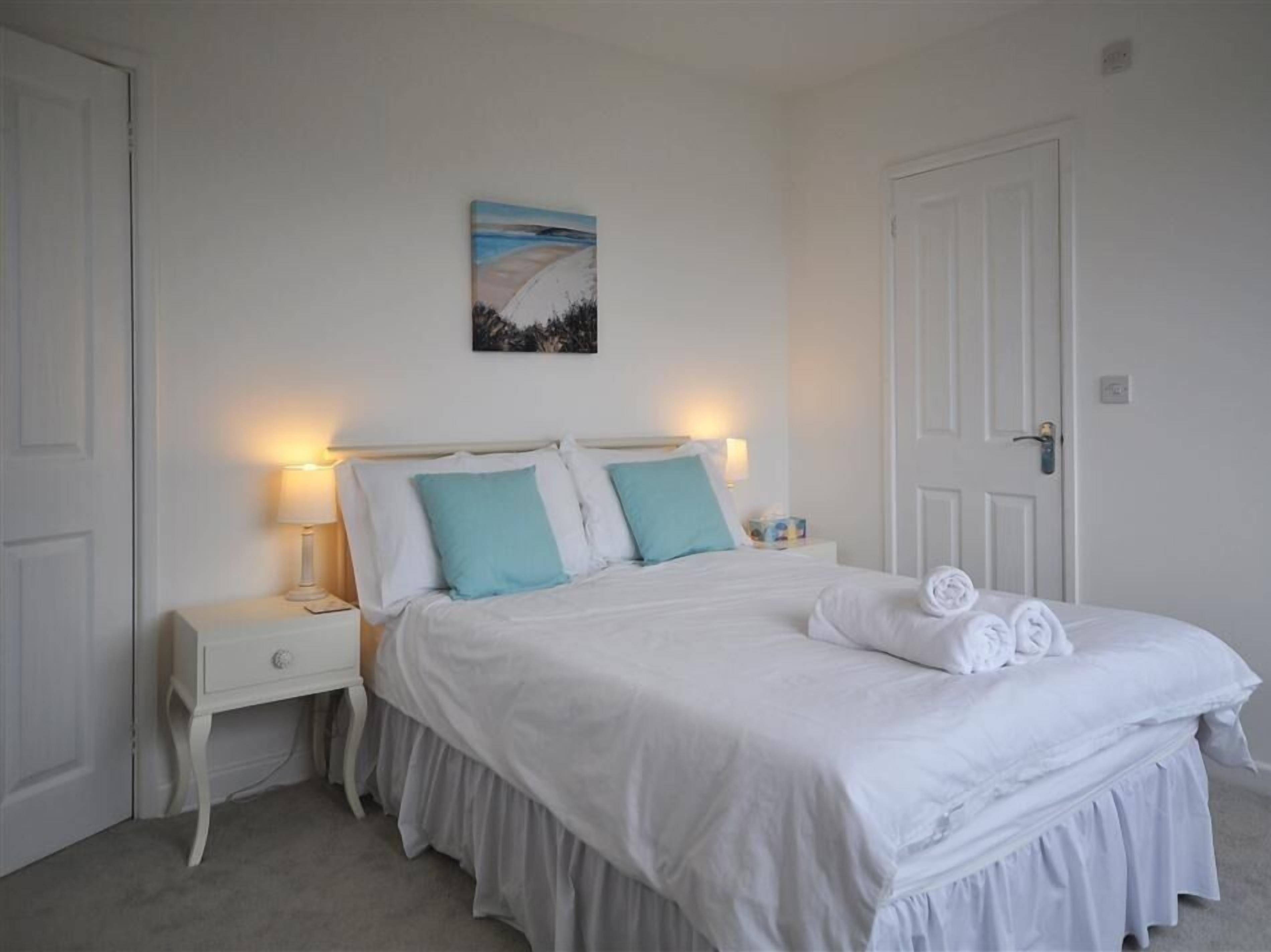 A bedroom with a bed, nightstands, a painting, and a door.