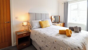 Una camera da letto ordinata con un letto, comodini, uno specchio e una finestra con tende.