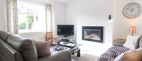 Ett vardagsrum med en soffa, en tv, en öppen spis och en klocka på väggen.