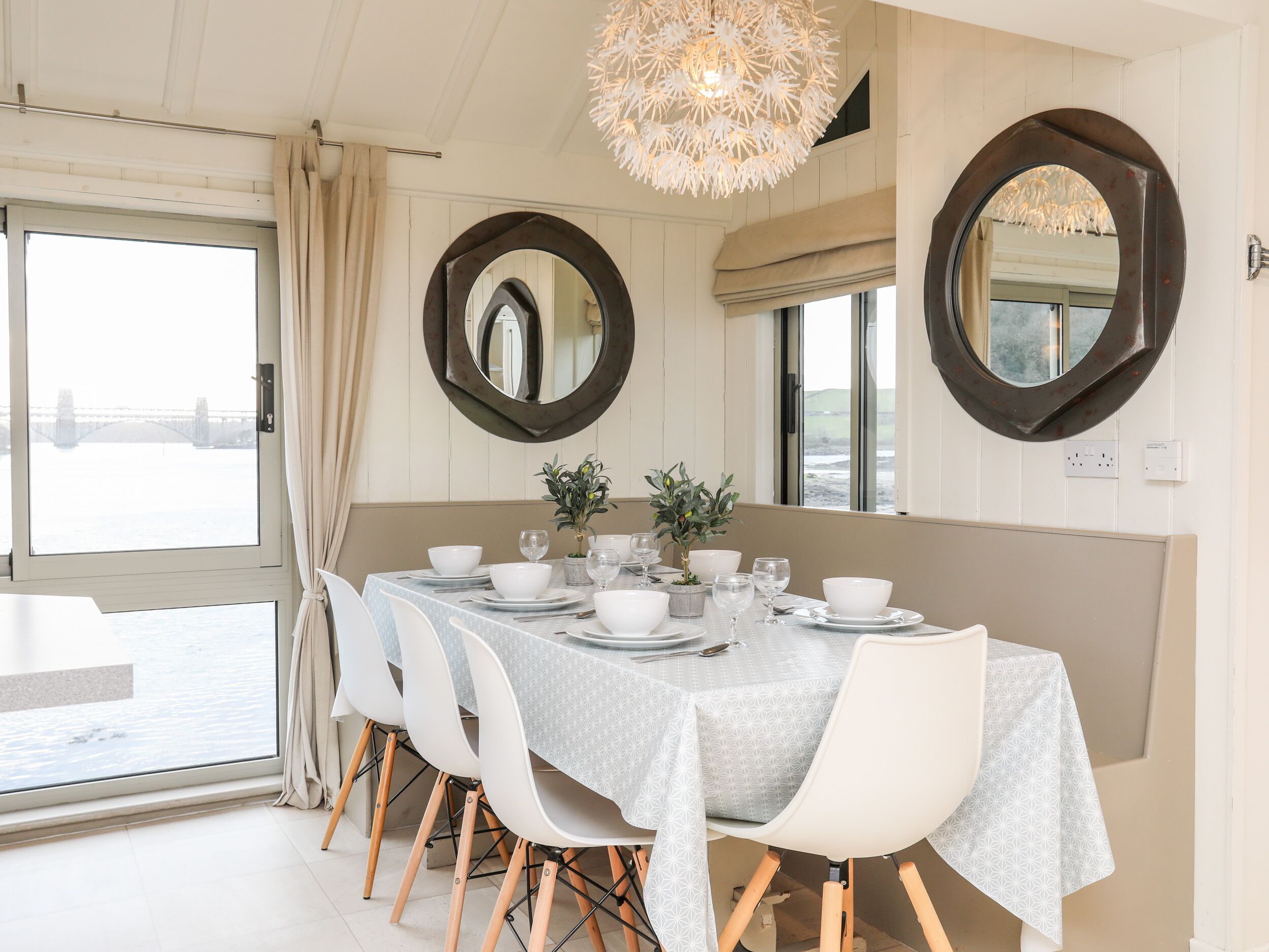 A dining area with a table set for four, white chairs, and two large mirrors on the walls.