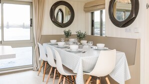 Un coin repas avec une table dressée pour quatre personnes, des chaises blanches et deux grands miroirs accrochés aux murs.