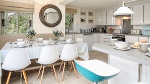 Une cuisine moderne avec des meubles blancs, un coin repas agrémenté d’un miroir rond et une vue sur la verdure à l’extérieur.