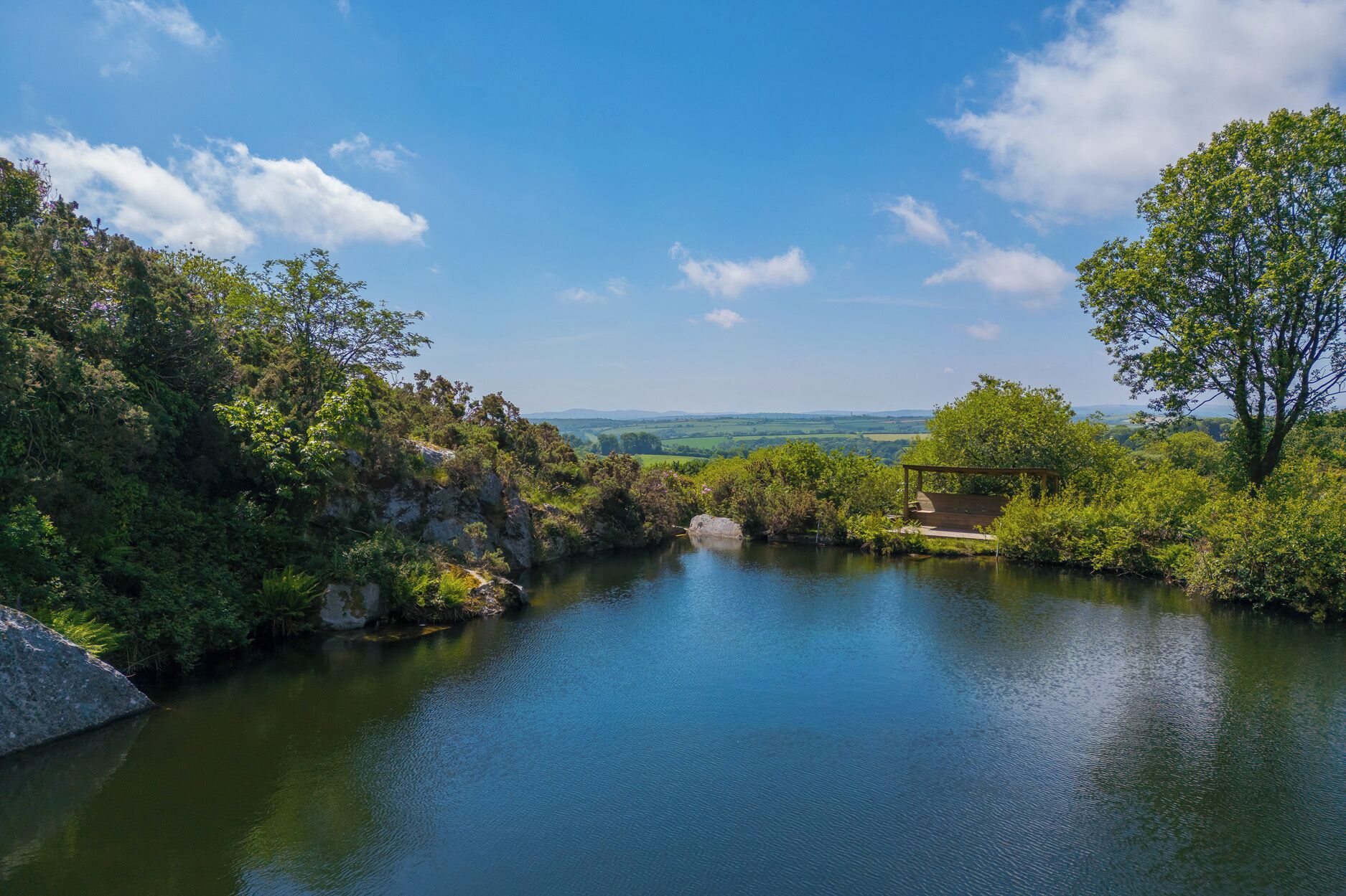 Ein friedlicher Blick auf ein Flussufer mit einer Holzanlage in der N ähe des Wassers, umgeben von üppigem Grün und Bäumen.