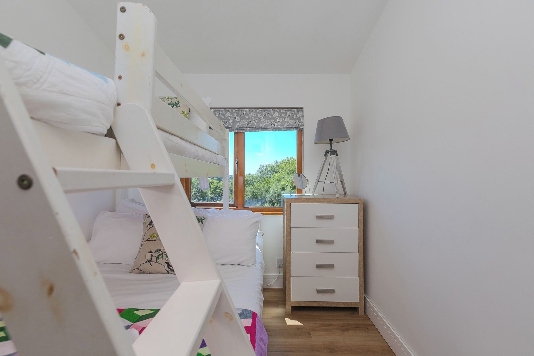 A bunk bed room with a window, a bedside lamp, and a wooden dresser.