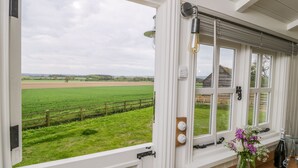 A room with a large window overlooking a green field, a wooden table with a vase of flowers, and a bottle of champagne. - Bellwether (York)
