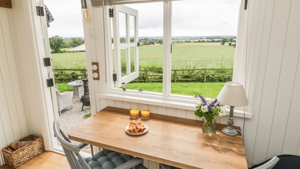 A kitchen with a wooden table, two chairs, a window with a view of a green field, and a lamp on the table. - Bellwether (York)