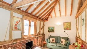 A cozy room with exposed wooden beams, a brick fireplace, a green sofa, and a television on a wooden table. - Pond View (Fordingbridge)