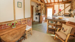 A rustic kitchen with exposed wooden beams, a brick wall, and a wooden dining table with chairs. - Pond View (Fordingbridge)