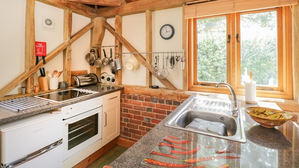 A kitchen with wooden beams, a stove, a sink, and a window with a view of greenery. - Pond View (Fordingbridge)