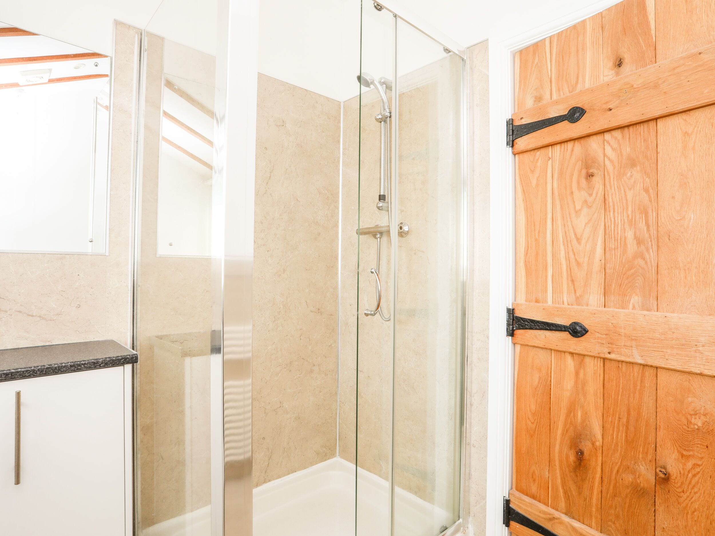 A modern bathroom with a glass shower enclosure, wooden door, and a white countertop.