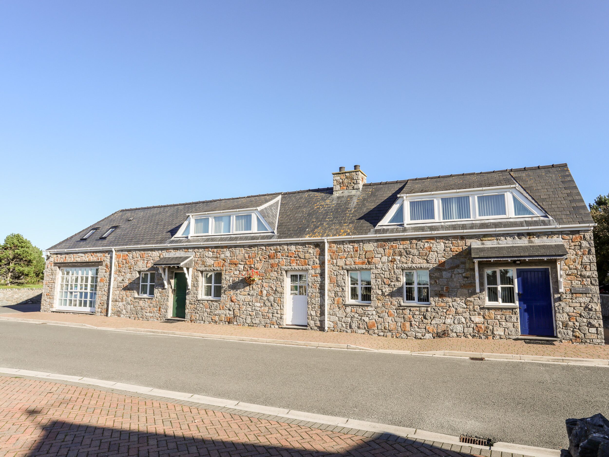 A stone building with a gabled roof, two windows with white frames, and a blue door.