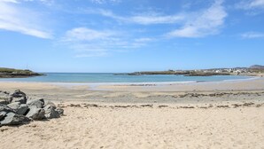 Une plage avec un ciel dégagé, un premier plan rocheux et des bâtiments situés au loin.