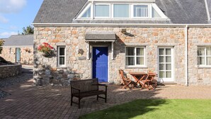 Une maison en pierre avec une porte bleue, un petit patio avec un banc et une table entourée de chaises.