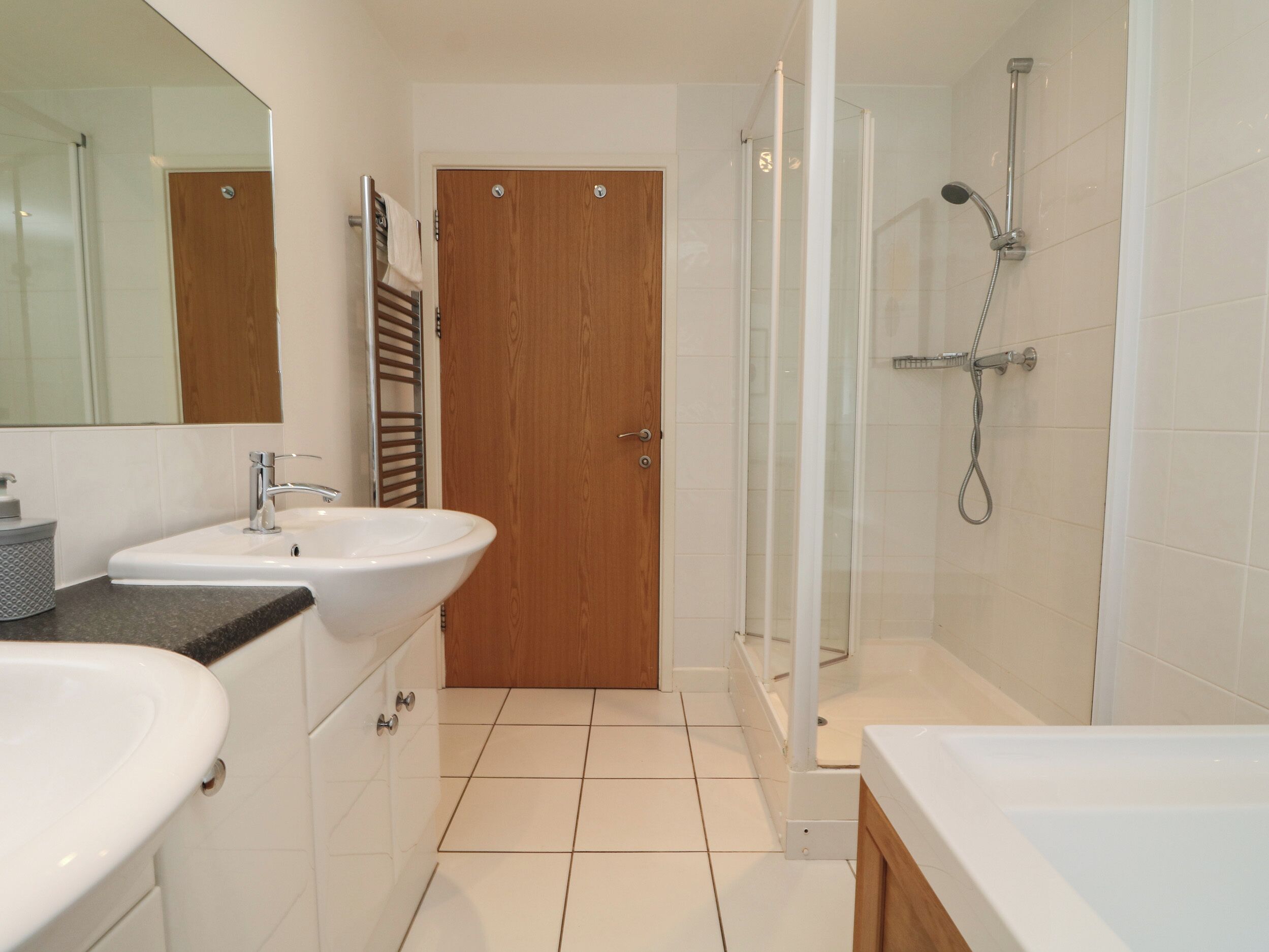 Un bagno con due lavabi, una doccia e una porta in legno.