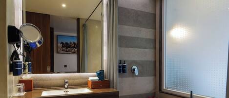 A modern bathroom with a large mirror, a bathtub filled with rose petals, and a window with frosted glass.