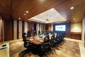 A conference room with a long table, multiple chairs, a projector screen, and a ceiling-mounted projector. - Radisson Blu Towers Kaushambi Delhi NCR (Ghaziabad)