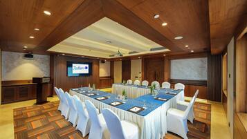 A conference room with a long table, white chairs, and a projector screen.
