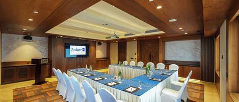 A conference room with a long table, white chairs, and a projector screen.