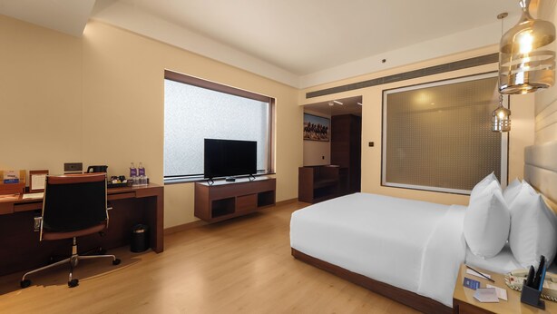 Ein Hotelzimmer mit einem Bett, einem Schreibtisch mit Computer, einem Fernseher und einem Fenster.