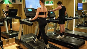 A gym with treadmills, a mirrored wall, and a large screen displaying a workout program. - Radisson Blu Towers Kaushambi Delhi NCR (Ghaziabad)