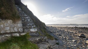 Una playa rocosa con una escalera de piedra que baja hacia la orilla.