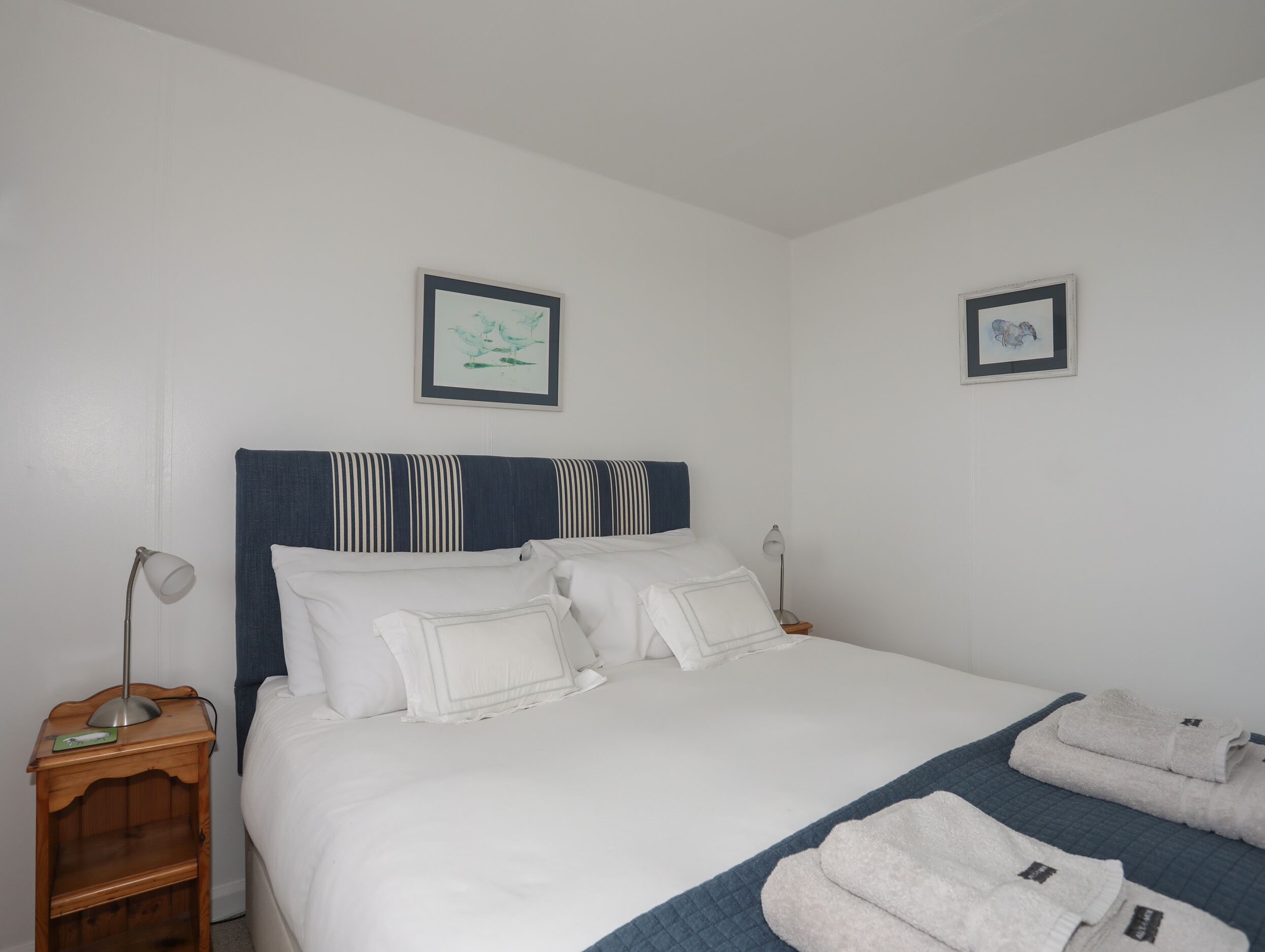 A neatly made bed with white linens, a striped headboard, and two framed pictures on the wall.
