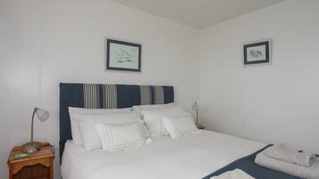 A neatly made bed with white linens, a striped headboard, and two framed pictures on the wall.