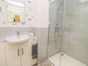 A bathroom with a white sink, a mirror with lights, a towel rack, and a glass shower enclosure. - Lambs Lodge (Bamburgh)